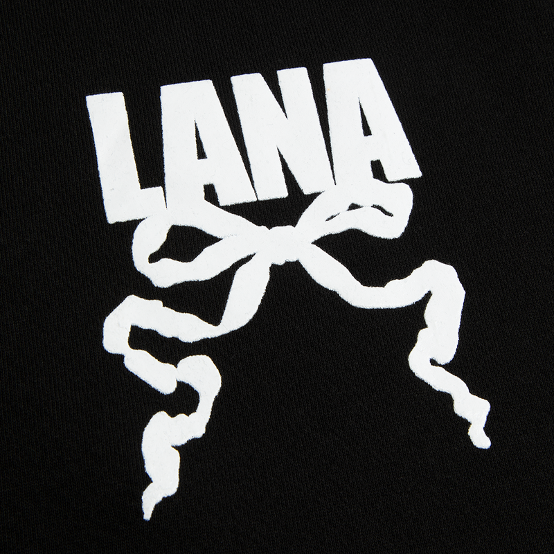 Close-up detail of the Lana Del Rey Logo Black Zip-Up Hoodie showcasing the white LANA logo with ribbon bow artwork printed on black cotton fleece, highlighting the minimalist vintage-inspired graphic design.