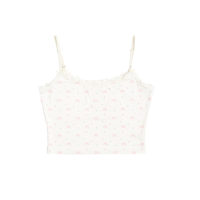Front view of the Bow Print Cropped Cami Tank Top featuring an ivory cropped camisole with adjustable spaghetti straps, delicate lace trim, and an all-over pink ribbon bow and pastel heart print inspired by Lana Del Rey's romantic aesthetic.