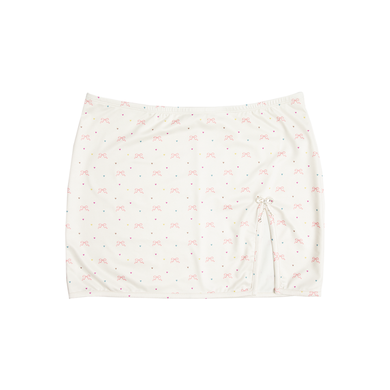 Front view of the Bow Print Mini Skirt featuring an ivory fabric with an all-over pink ribbon bow and pastel heart print, finished with a side drawstring and a sparkling rhinestone bow charm for a romantic Lana Del Rey-inspired look.