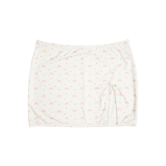 Front view of the Bow Print Mini Skirt featuring an ivory fabric with an all-over pink ribbon bow and pastel heart print, finished with a side drawstring and a sparkling rhinestone bow charm for a romantic Lana Del Rey-inspired look.