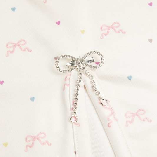 Close-up detail of the Bow Print Mini Skirt showcasing the sparkling rhinestone bow charm with adjustable drawstring on ivory fabric printed with delicate pink ribbon bows and pastel heart motifs.
