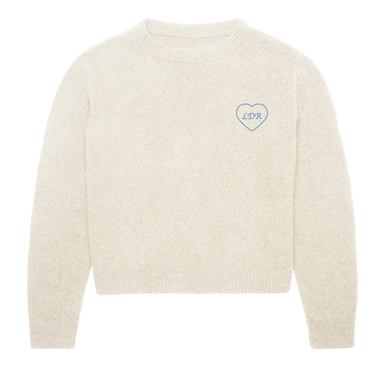 Front view of the Lana Del Rey Indio Ivory Knit Crewneck Sweater featuring a soft ivory knit construction with an embroidered blue LDR heart logo on the chest, premium heavyweight sweater inspired by Lana Del Rey's Indio festival merch collection.
