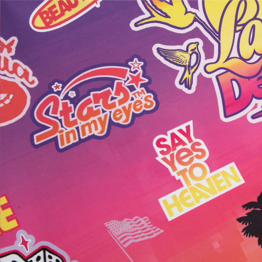 Close-up detail of the Paradise Print Biker Shorts showcasing colorful Stars in My Eyes, Say Yes to Heaven, bird illustration, and retro-inspired Lana Del Rey graphics printed on a vibrant pink and purple gradient fabric.